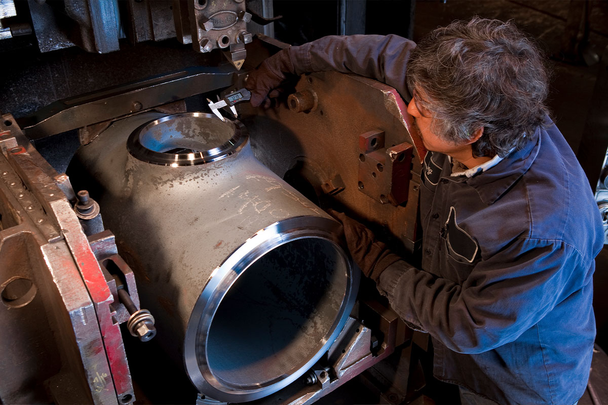 Technician measuring a machined heavy-wall forged tee fitting with calipers