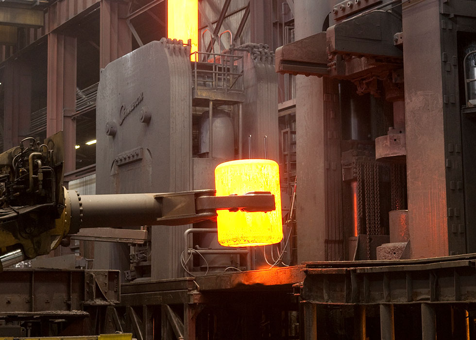 Glowing billet held in a forging manipulator in front of a press