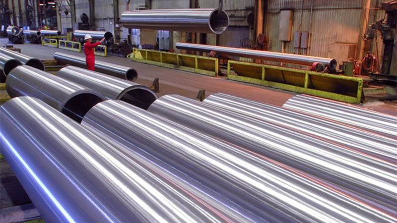 Worker guiding a large extruded pipe on an overhead crane in the mill